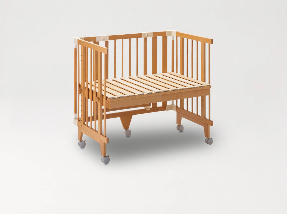 Creative Cot in co-sleeping mode: slatted base raised to the parent bed, one long side removed, on castors