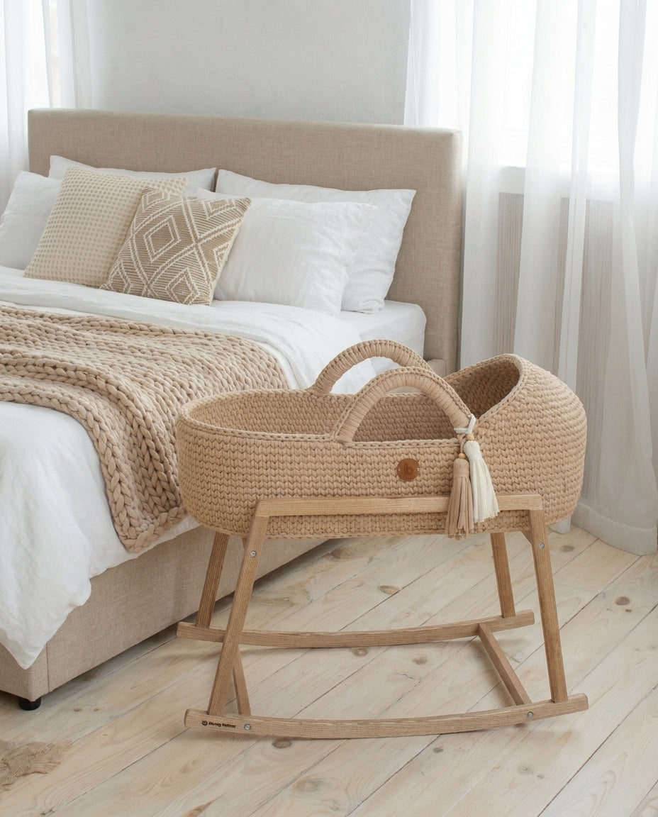 Handwoven Moses basket on a wooden rocking stand beside a parent bed