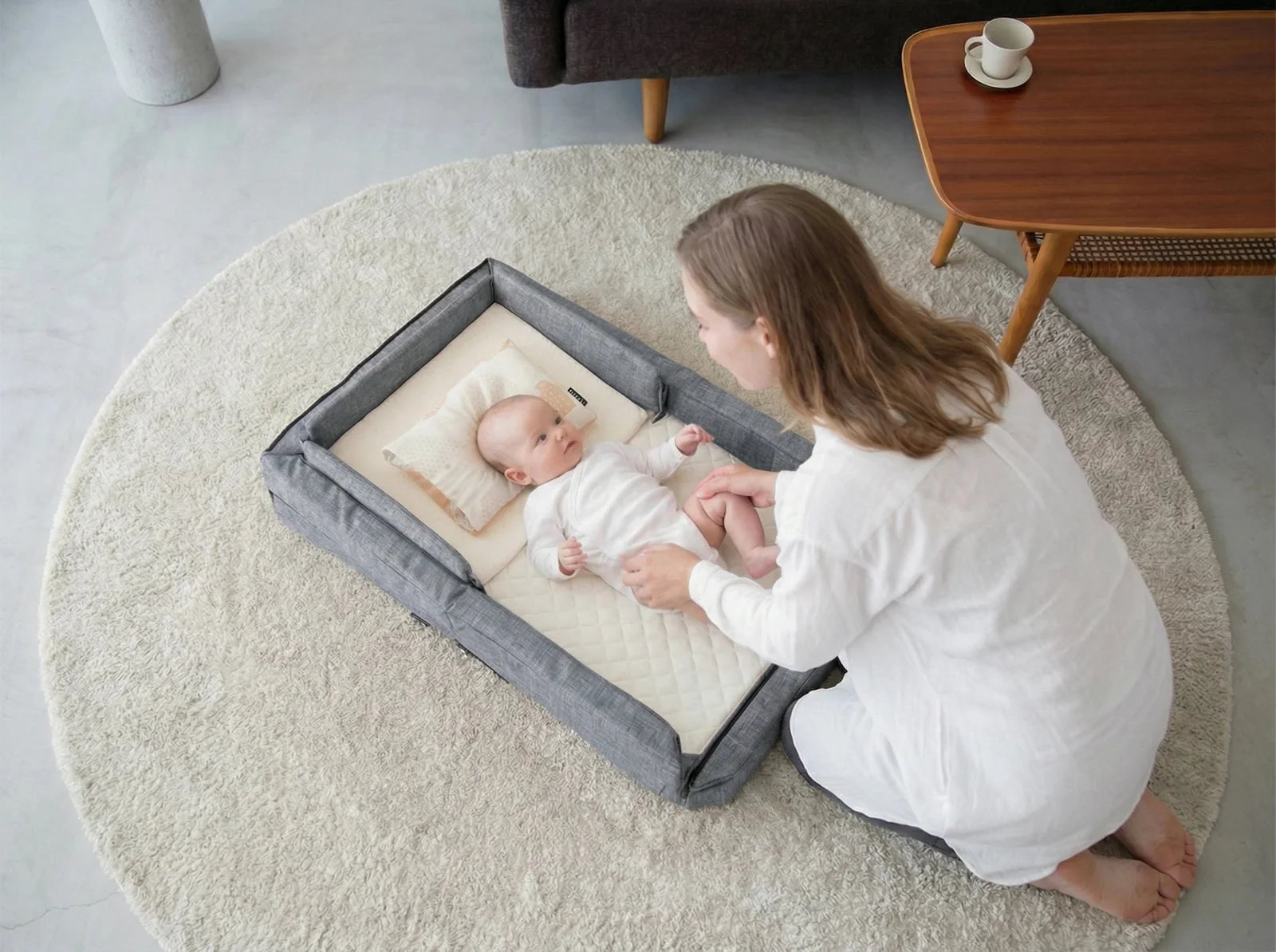 A baby lying calmly in the Compact Bed Free with raised bumpers beside mum
