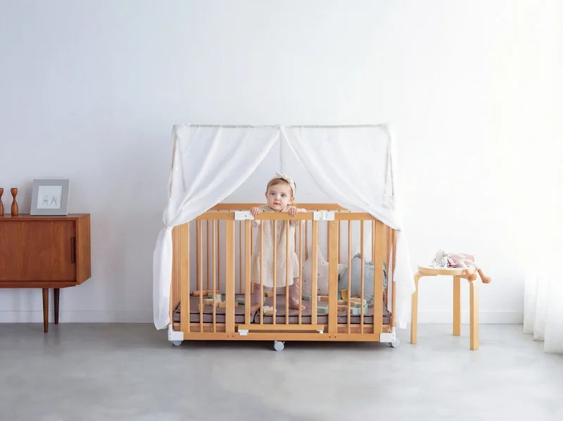 A baby standing in the Creative Cot Long playpen with a canopy