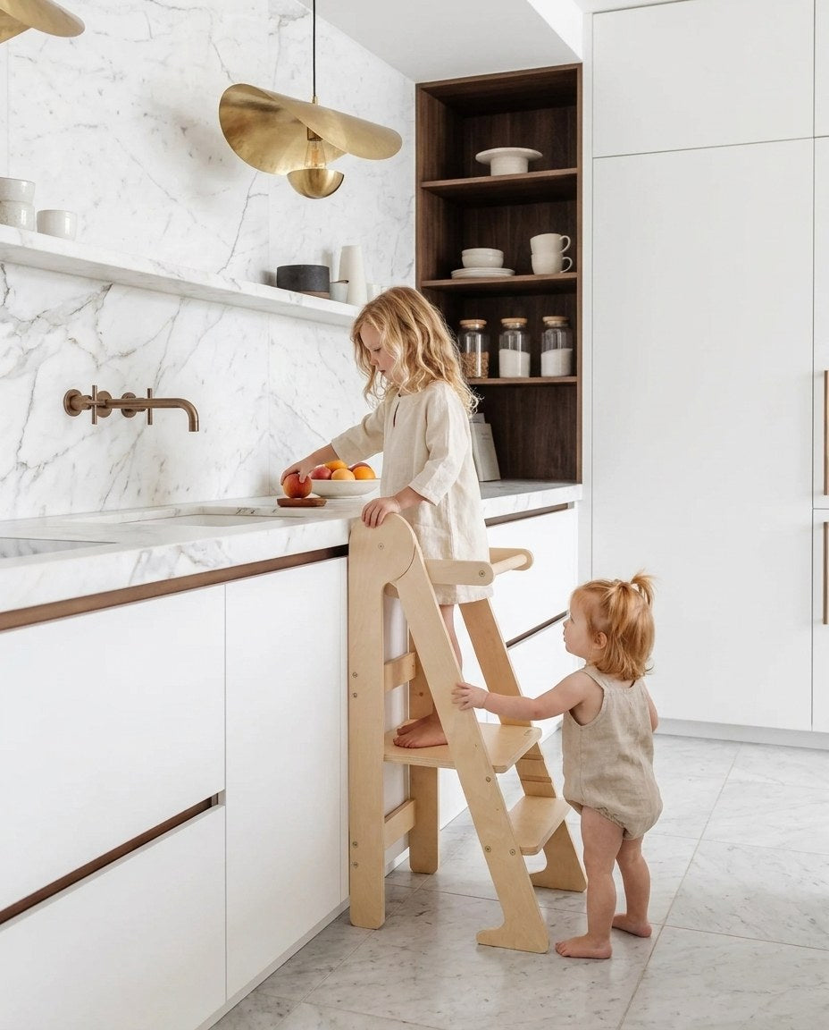 Two children on a learning tower by a marble countertop with fruit