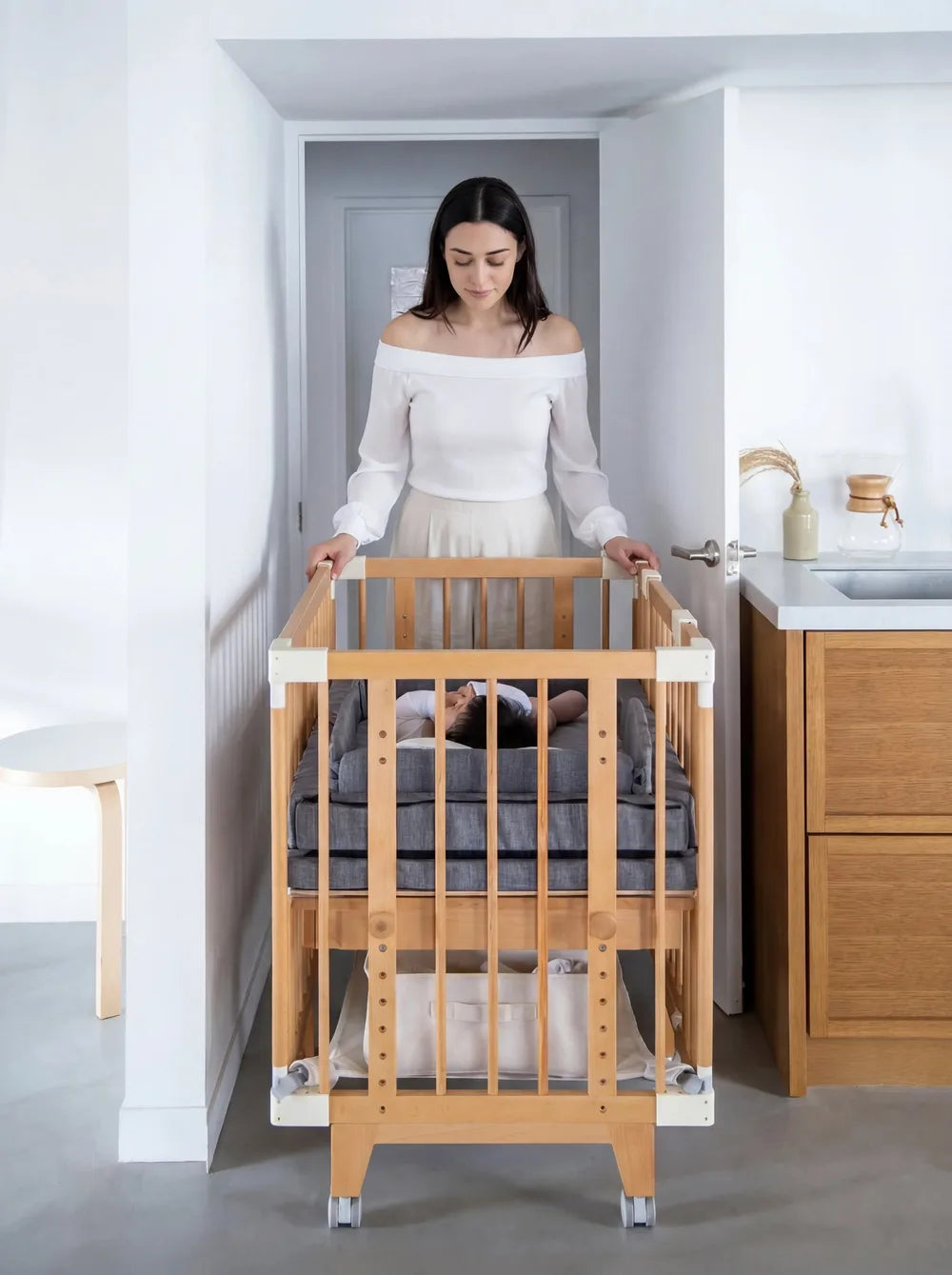 A mother wheeling the Creative Cot with her baby through a doorway
