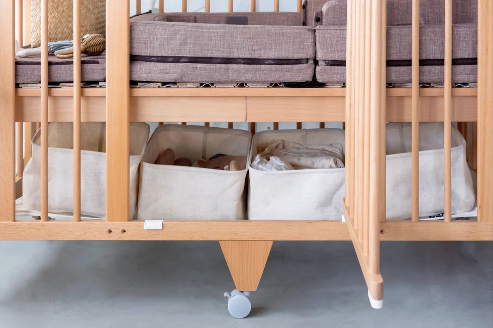 Baskets with kids' belongings in the space under the Creative Cot Long base
