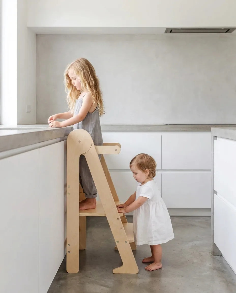 Two children on an ikiddoo learning tower in a bright kitchen